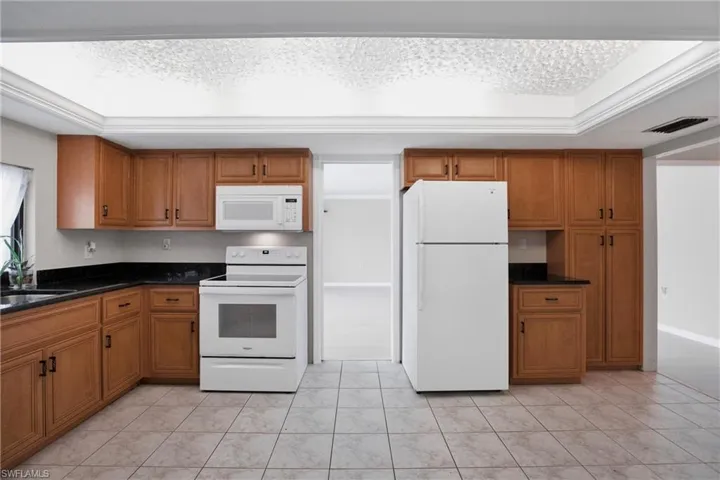 Kitchen with dark stone counters, sink, white appliances, and light tile patterned floors