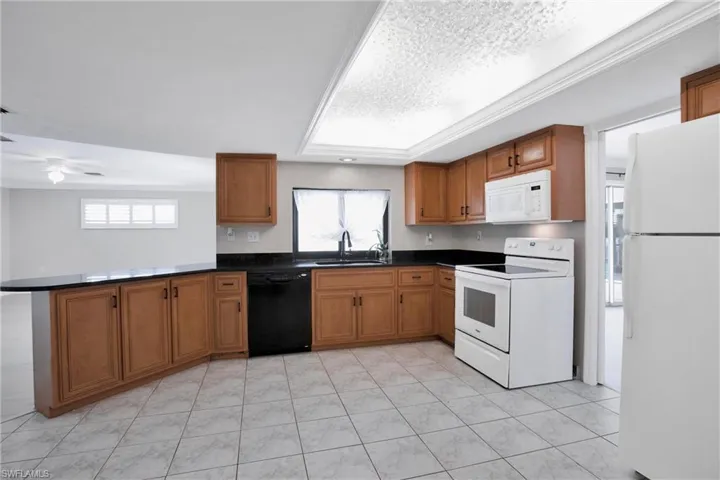 Kitchen with ceiling fan, white appliances, light tile patterned floors, and kitchen peninsula