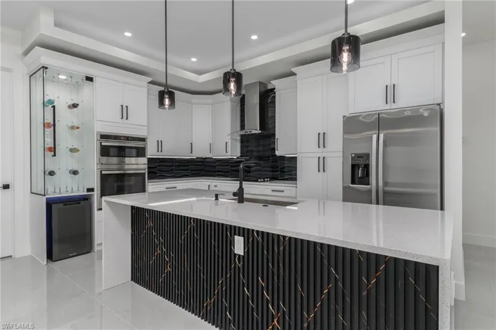 Kitchen featuring white shaker cabinetry, stainless steel appliances, a black textured backsplash, and a waterfall-edge island with a fluted and veined facade
