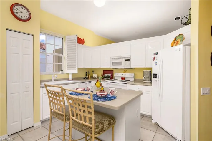 Kitchen with a center island, white appliances, white cabinets, light tile patterned floors, and a breakfast bar area
