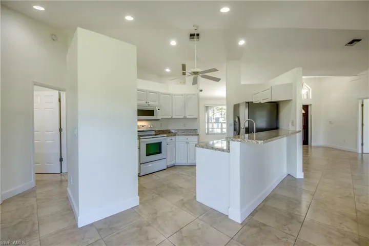 Kitchen with white appliances, white cabinets, a peninsula, light stone countertops, and recessed lighting