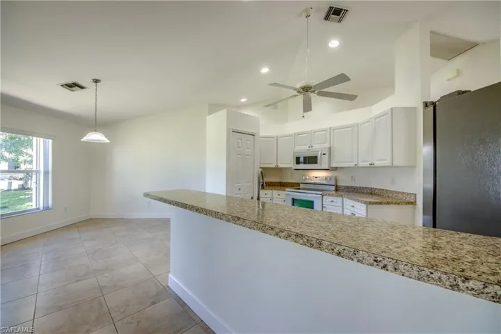 Kitchen featuring white appliances, white cabinetry, light countertops, lofted ceiling, and decorative light fixtures
