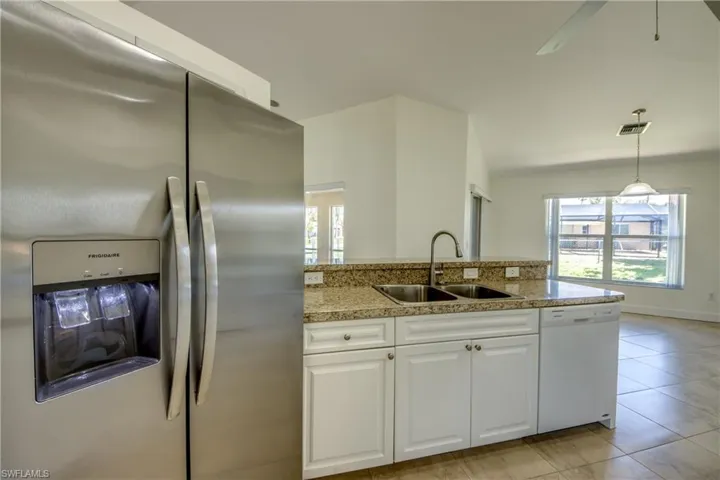 Kitchen featuring stainless steel fridge, dishwasher, healthy amount of natural light, white cabinetry, and lofted ceiling