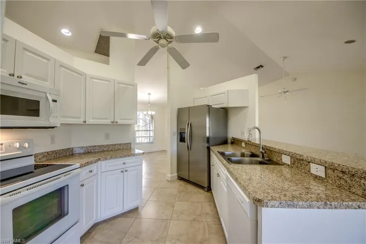 Kitchen with white appliances, a ceiling fan, white cabinets, a peninsula, and light tile patterned flooring