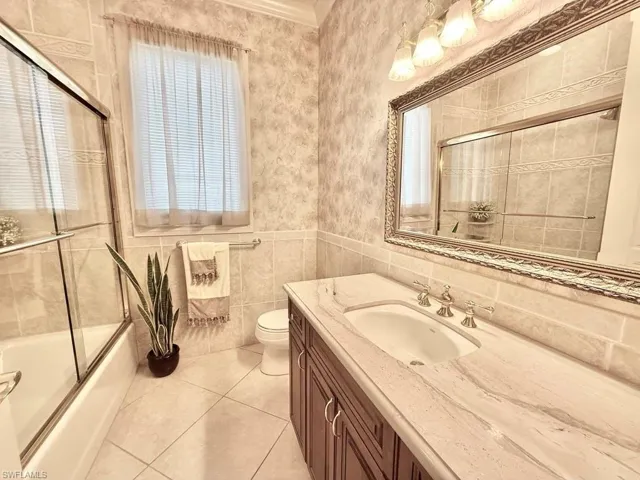 Full bathroom featuring toilet, combined bath / shower with glass door, crown molding, vanity, and tile patterned flooring