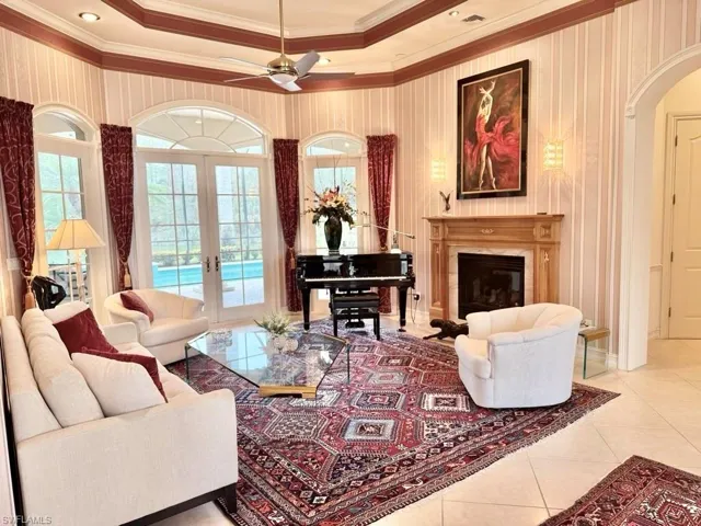 Living room with light tile patterned floors, crown molding, a high end fireplace, french doors, and a raised ceiling