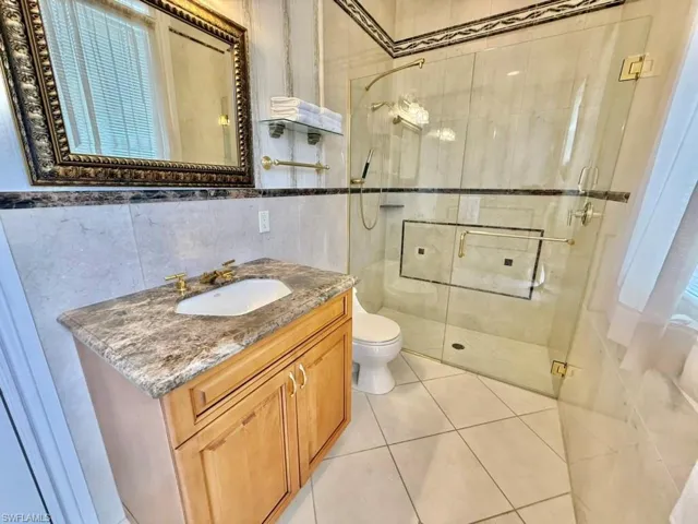 Bathroom with toilet, an enclosed shower, tile walls, vanity, and tile patterned flooring