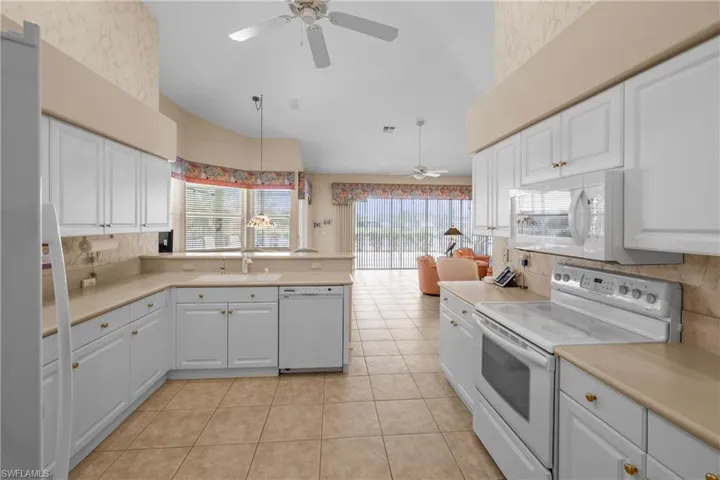 Kitchen featuring white appliances, sink, hanging light fixtures, white cabinetry, and light tile floors