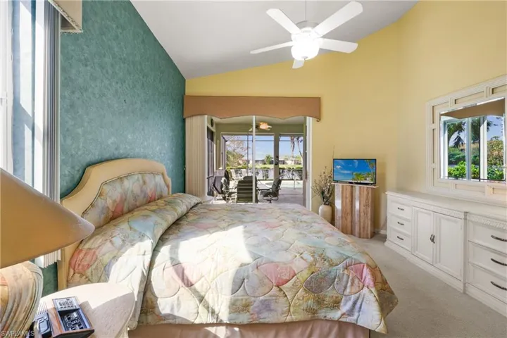 Primary bedroom with light carpet, lofted ceiling, sliding glass doors to pool lanai, and ceiling fan