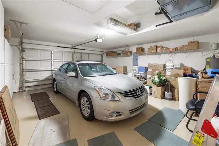 Garage featuring a garage door opener, electric panel, storage cabinets and shelving and water heater