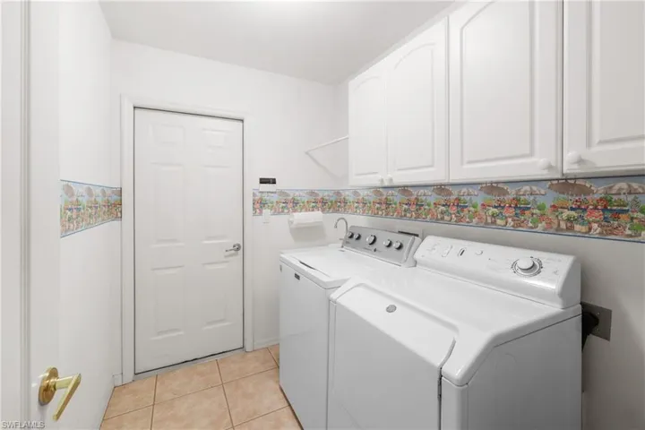 Laundry area featuring light tile flooring, washer and dryer, laundry sink and upper cabinets