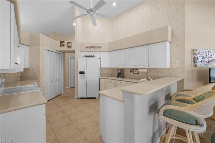 Kitchen featuring a towering ceiling, white refrigerator with ice dispenser, kitchen peninsula, white cabinets, and light tile floors