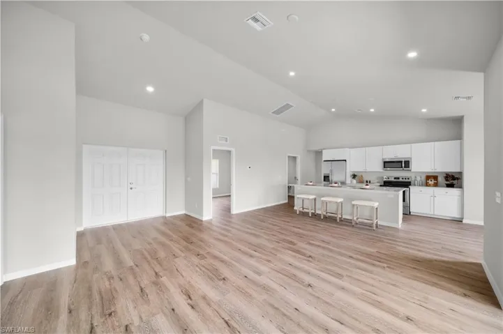 Unfurnished living room with light wood-type flooring, high vaulted ceiling, baseboards, and visible vents