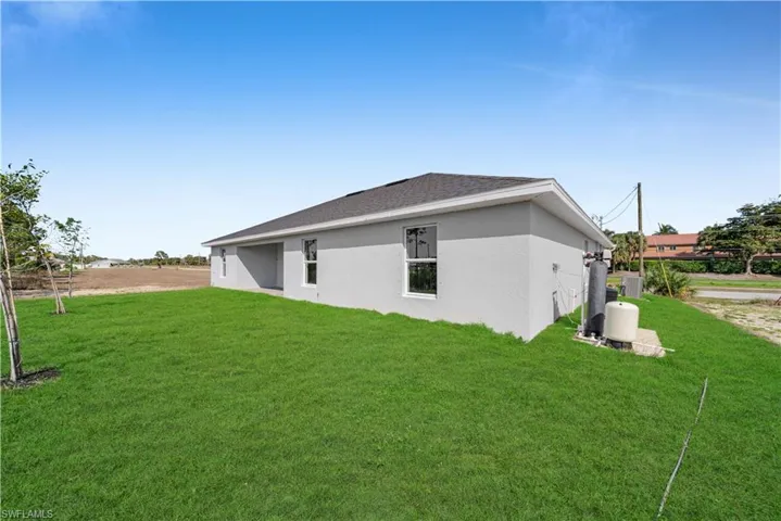 Rear view of house with stucco siding, a shingled roof, and a yard