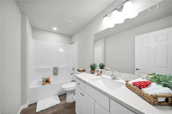 Bathroom with bathtub / shower combination, visible vents, toilet, vanity, and wood finished floors