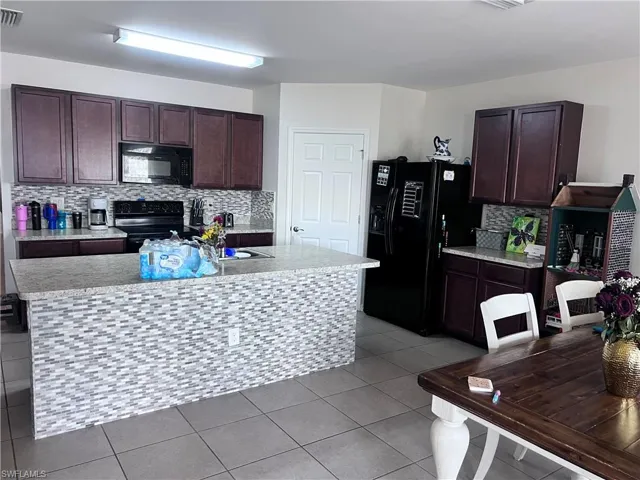 Kitchen featuring a center island with sink, decorative backsplash, black appliances, dark wood finish cabinets, and light tile patterned floors