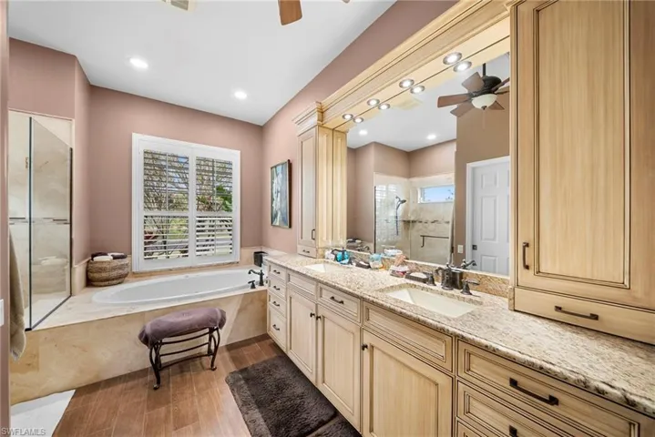 Bathroom featuring a stall shower, vanity, a ceiling fan, dark wood-type flooring, and a garden tub