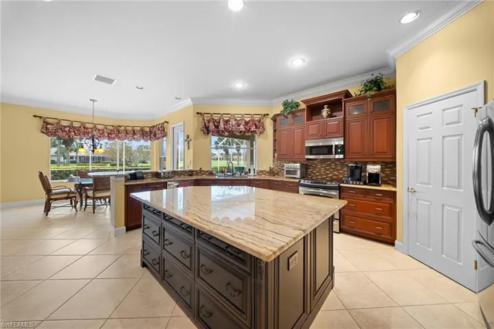 Kitchen featuring a peninsula, light stone counters, decorative backsplash, a center island, and crown molding
