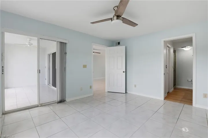 Unfurnished bedroom featuring ceiling fan, access to exterior, light tile patterned floors, and ensuite bath