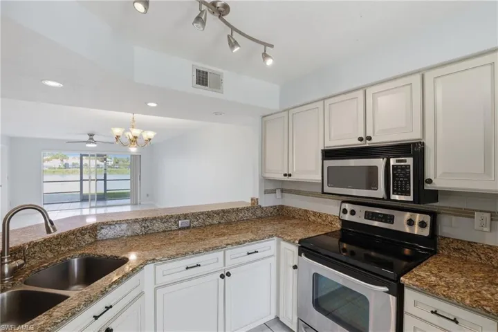 Kitchen featuring stainless steel appliances, dark stone counters, ceiling fan, hanging lights, and white cabinetry