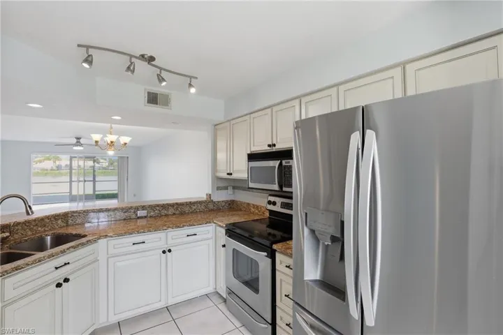 Kitchen with stainless steel appliances, dark stone counters, light tile patterned floors, suspended lighting, and a ceiling fan