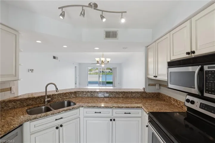 Kitchen with stainless steel appliances, hanging lights, dark stone counters, white cabinets, and a peninsula