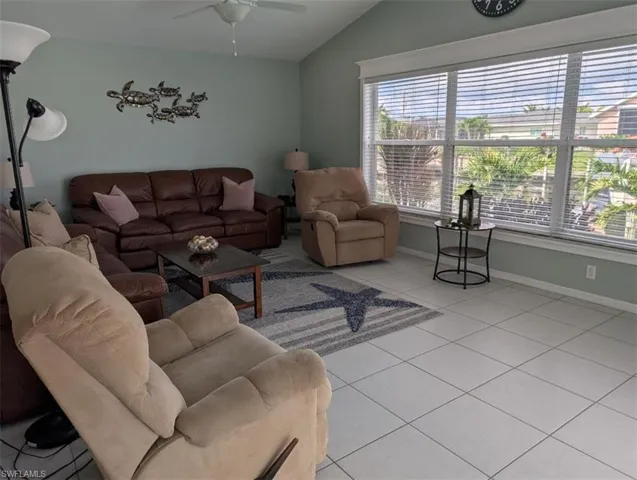 Living room featuring light tile patterned floors, vaulted ceiling, a ceiling fan, and baseboards