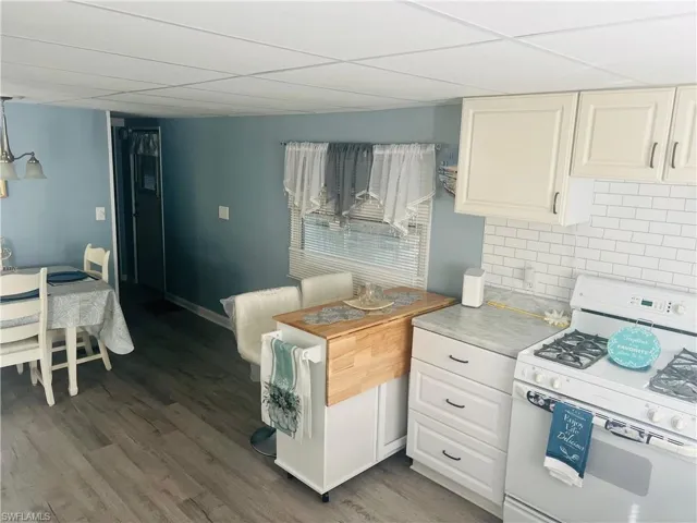 Kitchen with white range with gas cooktop, a paneled ceiling, tasteful backsplash, light countertops, and light wood finished floors