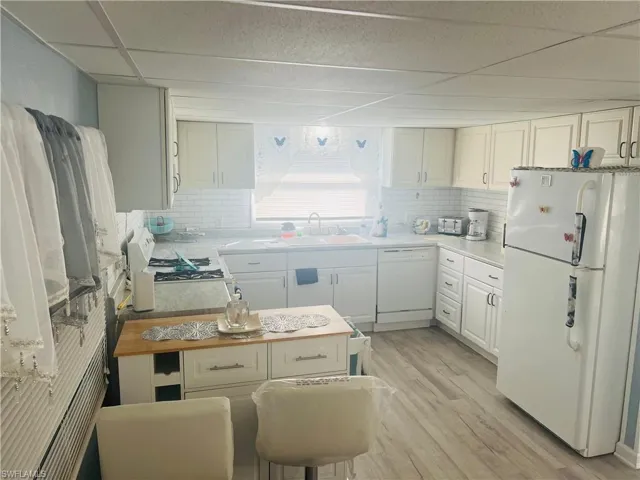 Kitchen with white appliances, white cabinets, light wood finished floors, light countertops, and a paneled ceiling