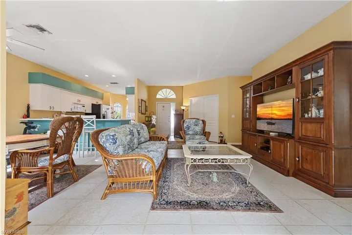 Open-concept living area featuring light-toned tile flooring, a built-in media cabinet with display shelving, and vaulted ceilings