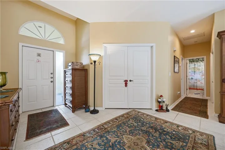 Foyer featuring light-toned tile flooring, a half-round transom window, and a vaulted ceiling