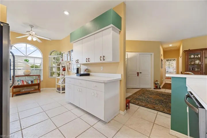 Kitchen area featuring white cabinetry, light-toned tile flooring, and a large arched window with horizontal blinds