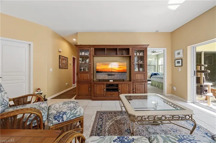 Spacious living area featuring light-toned tile flooring, vaulted ceiling, and built-in wood cabinetry with glass-front display sections