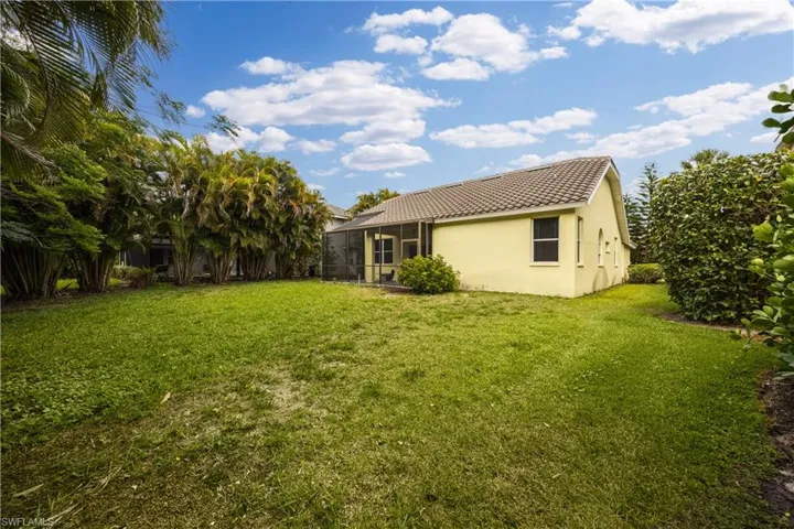 Expansive grassy backyard featuring perimeter landscaping, a screened patio, and a tiled roofline
