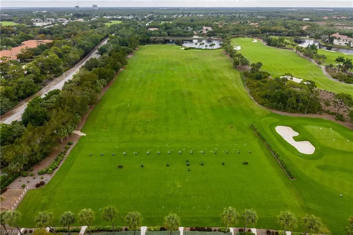 Expansive driving range featuring multiple teeing areas, bordered by mature trees and a manicured golf course