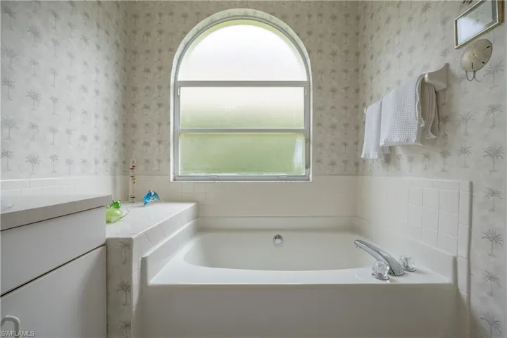 Soaking tub with chrome fixtures, arched window, and built-in storage cabinetry