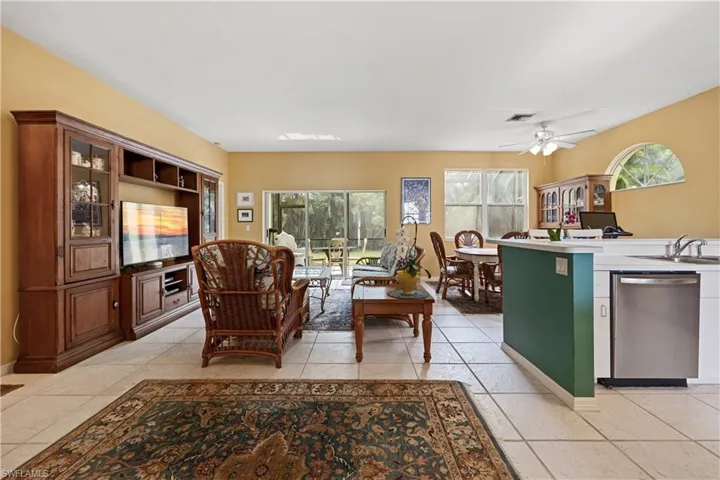 Light-toned tile flooring extends throughout this open-concept area featuring a kitchen peninsula with stainless steel appliances, a ceiling fan, and multiple windows providing ambient illumination