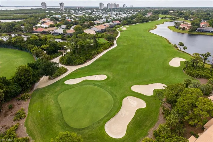 Expansive golf course green with sand traps, bordered by mature trees and a tranquil water feature