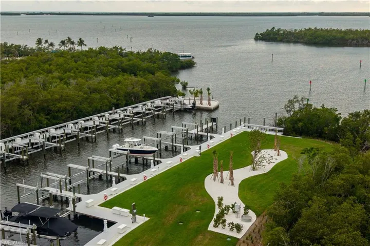 Expansive marina with multiple boat slips featuring boat lifts, direct water access, a manicured green space, and surrounding natural foliage