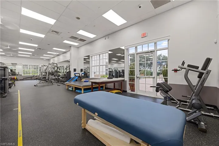 Spacious fitness area featuring rubberized flooring, mirrored walls, and ample natural light from large windows
