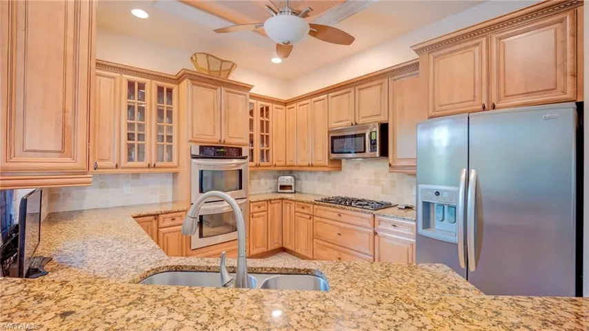 Kitchen featuring stainless steel appliances, light stone countertops, glass fronted cabinets, a ceiling fan, and recessed lighting