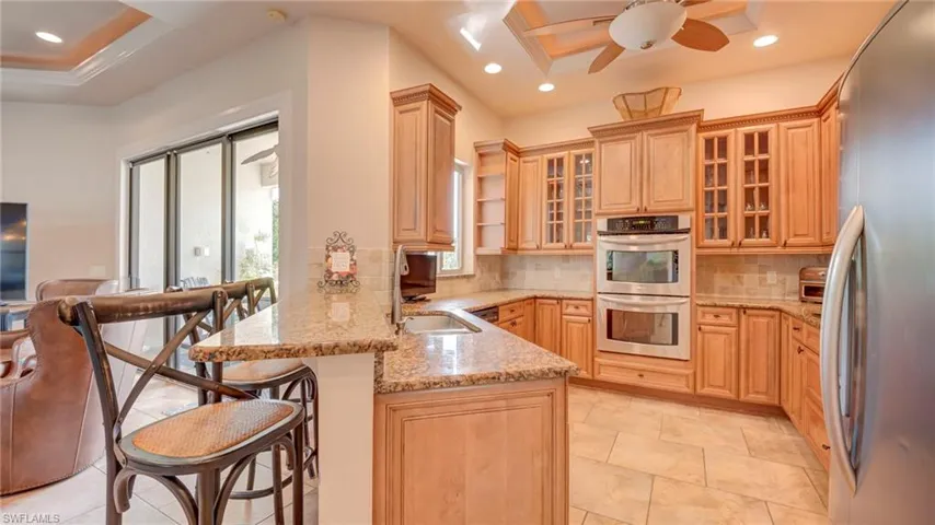 Kitchen with stainless steel appliances, a peninsula, light stone countertops, a breakfast bar, and recessed lighting
