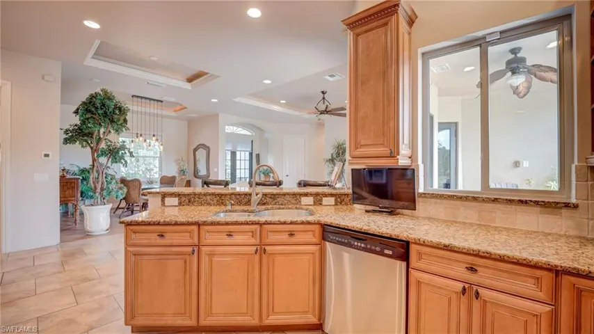 Kitchen featuring stainless steel dishwasher, ceiling fan, a tray ceiling, light stone counters, and crown molding