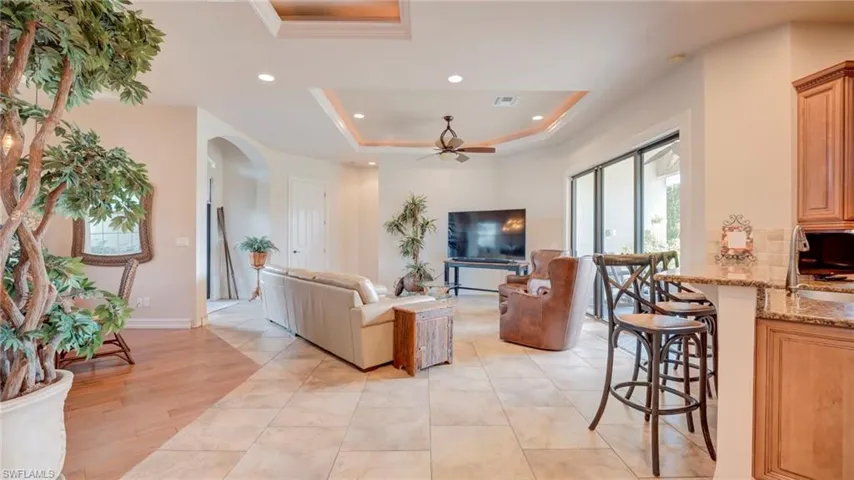 Living room featuring a raised ceiling, a ceiling fan, recessed lighting, arched walkways, and light tile patterned floors
