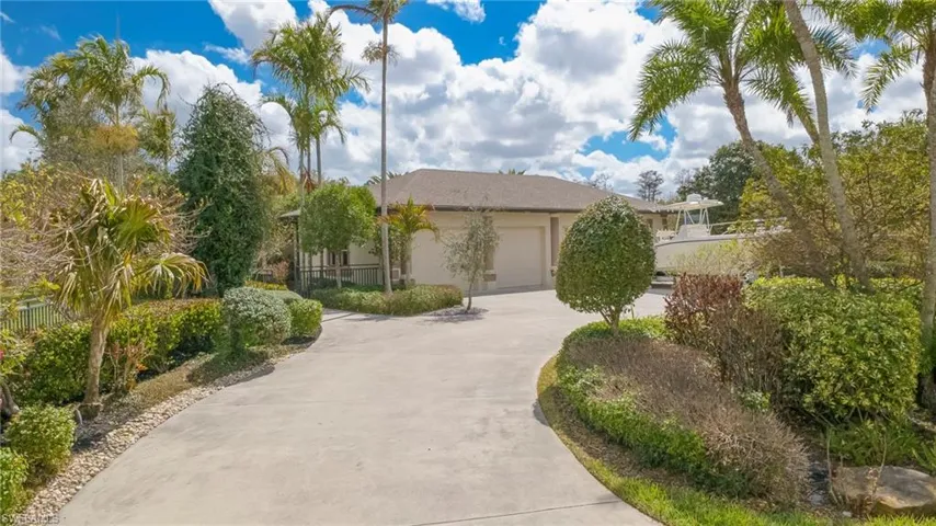 View of estate hidden behind natural elements with driveway, stucco siding, and a garage