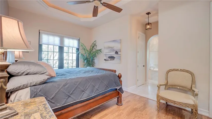 Primary Bedroom with crown molding, a raised ceiling, a ceiling fan, light wood-style flooring, and ensuite bathroom
