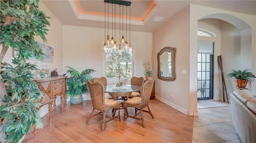 Dining area with a tray ceiling, light wood-type flooring, and arched walkways