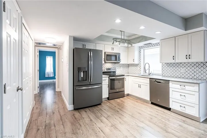 Kitchen featuring white cabinets, sink, light hardwood / wood-style flooring, appliances with stainless steel finishes, and a tray ceiling