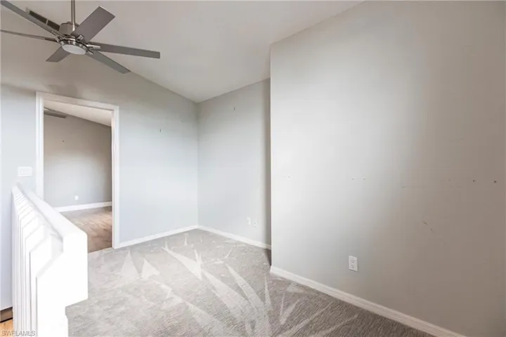 Empty room with ceiling fan, light carpet, and vaulted ceiling