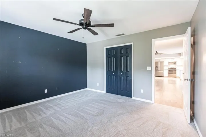 Unfurnished bedroom with stainless steel fridge, ceiling fan, a closet, and carpet